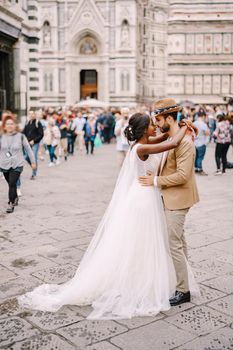 African-American bride and Caucasian groom cuddling in Piazza del Duomo. Wedding in Florence, Italy. Interracial wedding couple