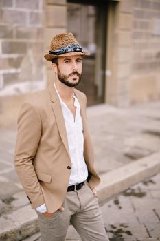 A young guy with a straw hat, a white unbuttoned shirt and a sand jacket, a small beard walks around of Florence.