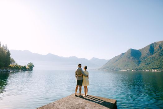A couple in love stands hugging on a pier in the Bay of Kotor near Perast against the backdrop of mountains, back view. High quality photo