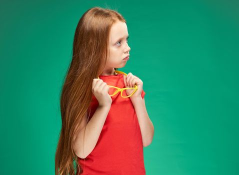 red-haired girl holding glasses in her hands red t-shirt emotions green background. High quality photo