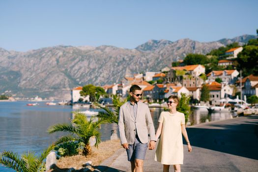 A loving couple walks holding hands along the embankment of the old town of Perast . High quality photo