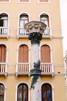 White column with an ornament against the background of a yellow building in Venice, Italy.