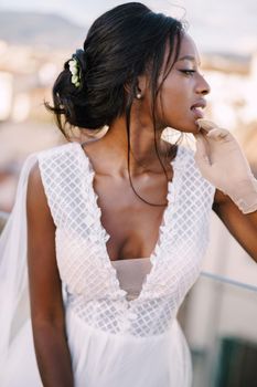 A beautiful African-American bride in white wedding dress, touches her face in vintage gloves. Fine-Art wedding in Florence, Italy