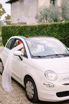 Beautiful bride and groom leaning forehead to forehead in a convertible in front of the old villa in Italy, in Tuscany, near Florence