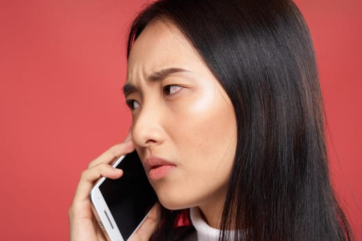 woman of asian appearance talking on the phone emotions dissatisfaction close-up red background. High quality photo