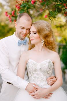 The bride and groom tenderly snuggle against the background of a flowering oleander bush near the ancient church in Prcanj . High quality photo