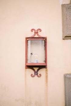 An ancient street lamp on a sand-colored wall.