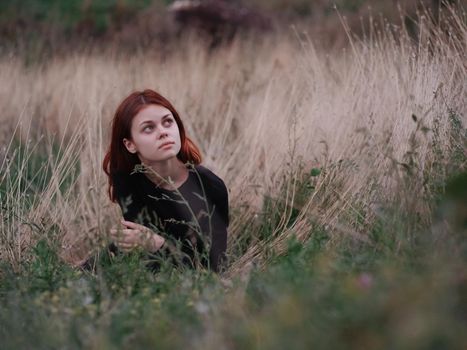 red-haired woman in a black dress lies in a field on dry grass in nature. High quality photo
