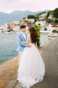 The bride and groom tenderly embrace on the seashore near the cozy old town of Perast in the Bay of Kotor . High quality photo