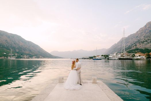 The bride in a wreath and groom hug on the pier near the old town of Kotor in the Bay of Kotor . High quality photo