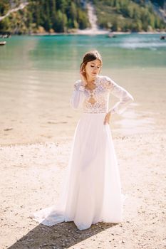 A beautiful bride in a white chiffon dress with sleeves and lace on the shores of Lake Lago di Braies in Italy. Destination wedding in Europe, on the popular Braies lake.