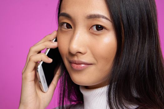 woman of asian appearance with a phone in hand communication close-up pink background. High quality photo