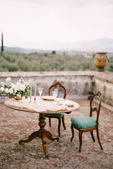 A wooden table and two old chairs, served and decorated for a wedding dinner.