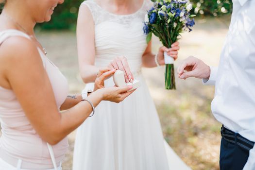 The bride takes a wedding ring from the box held by the bridesmaid to put it on the groom's finger . High quality photo