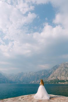 A beautiful blonde bride in a puffy white dress stands on a pier in the Bay of Kotor . High quality photo