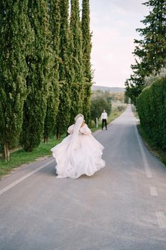 Wedding at an old winery villa in Tuscany, Italy. The bride runs on the way to the groom. A row of cypresses along the road.