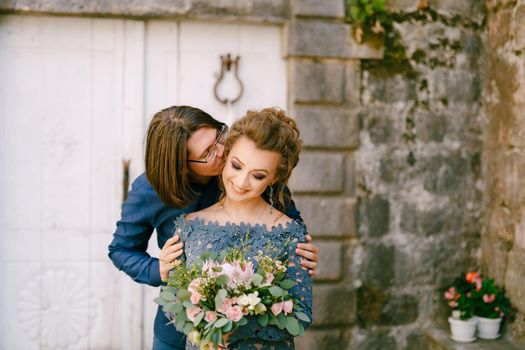 The groom kisses the bride on the cheek against the background of an old building with white doors in the old town of Perast . High quality photo