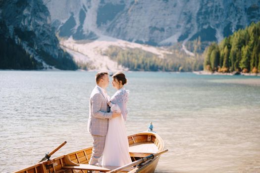 Bride and groom sailing in wooden boat, with oars at Lago di Braies lake in Italy. Wedding in Europe - Newlyweds are standing embracing in boat