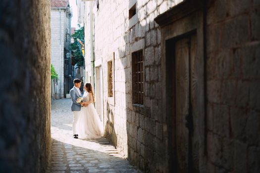 The bride and groom embracing on a beautiful old street of Perast in a narrow dark passage between houses . High quality photo