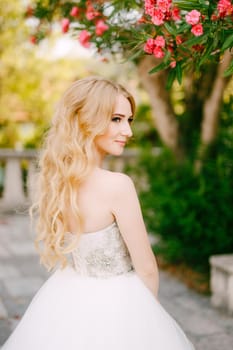 A graceful blonde bride stands under the branches of a blooming oleander near the ancient church in Prcanj . High quality photo