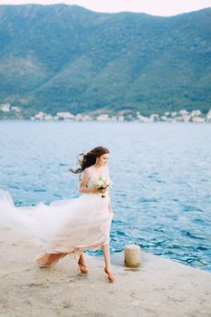 The bride holds a bouquet of roses in her hands and walks along the pier in the Bay of Kotor. High quality photo