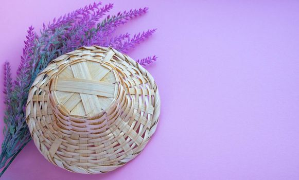 A basket in the shape of a hat lies on a branch of artificial lavender on a pink background. Space for your text.