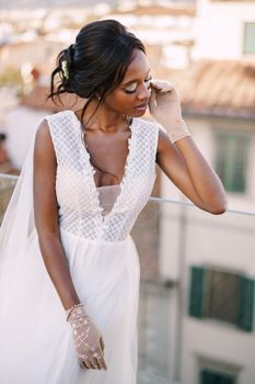 A beautiful African-American bride in white wedding dress, touches her face in vintage gloves. Fine-Art wedding in Florence, Italy