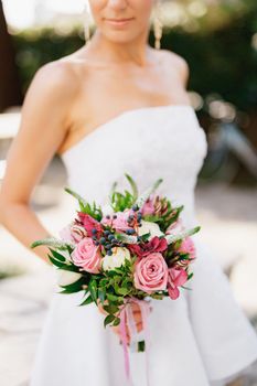 A sophisticated bride holding a wedding bouquet with roses, veronica, viburnum and boxwood in her hands, close-up . High quality photo