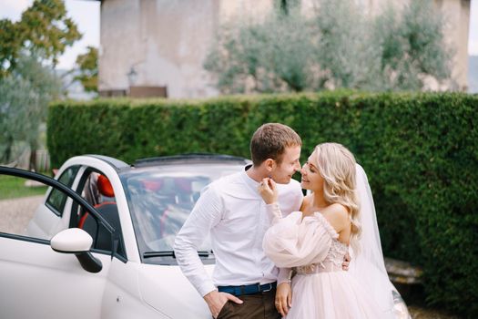 Beautiful bride and groom leaning on a convertible and looking at each other in front of the old villa in Italy, in Tuscany, near Florence