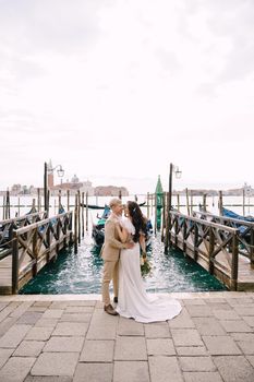 The groom and stand next to the pier for gondolas, hugging, in Venice, near the Piazza San Marco, overlooking San Giorgio Maggiore and the sunset sky. The largest pier for gondolas in Venice, Italy.