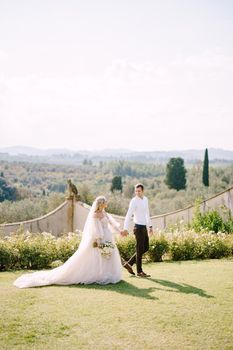 Wedding at an old winery villa in Tuscany, Italy. Round wedding arch decorated with white flowers and greenery in front of an ancient Italian architecture. The bride and groom walk in the park.