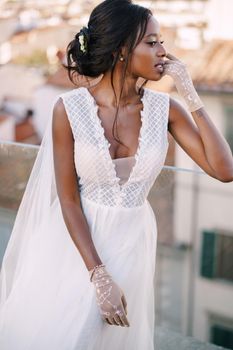 A beautiful African-American bride in white wedding dress, touches her face in vintage gloves. Fine-Art wedding in Florence, Italy