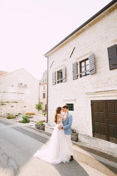 The bride and groom are embracing near the beautiful white house in the old town of Perast . High quality photo