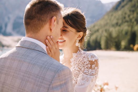 Newlyweds kiss on the spot for the ceremony, with an arch of autumn flower columns, against the backdrop of Lago di Braies in Italy. Destination wedding in Europe, at Braies lake.