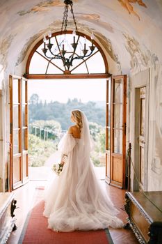 The bride walks in the interior of the villa, overlooking the garden. Wedding at an old winery villa in Tuscany, Italy.