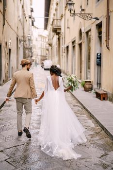 Interracial wedding couple. African-American bride and Caucasian groom walk down the street. Wedding in Florence, Italy