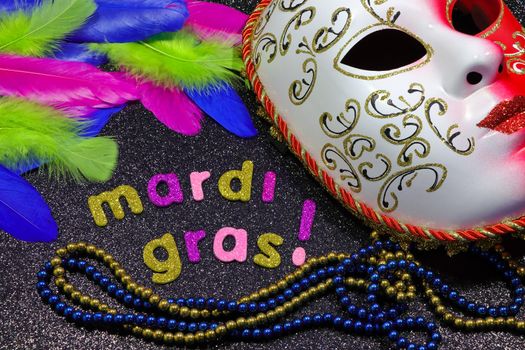 Mardi Gras text and beads with full carnival face mask and feathers on textured black