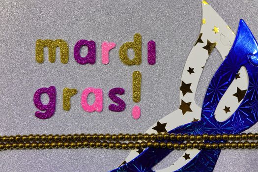 Mardi Gras text with party masks and bead string on textured silver surface