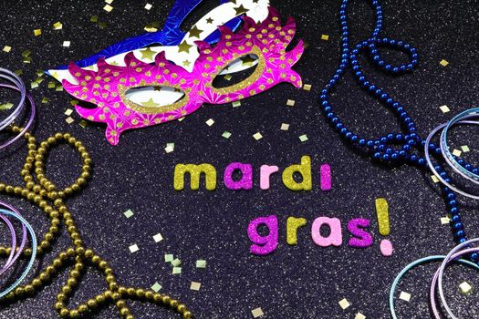 Mardi Gras text and confetti with party masks and jewelry on textured black