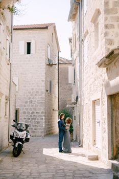 Bride in stylish blue dress and the groom hugging against the background of beautiful white houses in the old town of Perast, . High quality photo