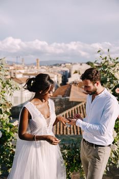 Interracial wedding couple. Destination fine-art wedding in Florence, Italy. A wedding ceremony on the roof of the building, with cityscape views of the city and Cathedral of Santa Maria Del Fiore