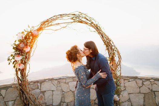 The bride and groom hugging and kissing near the wedding arch on the observation deck overlooking the Bay of Kotor . High quality photo