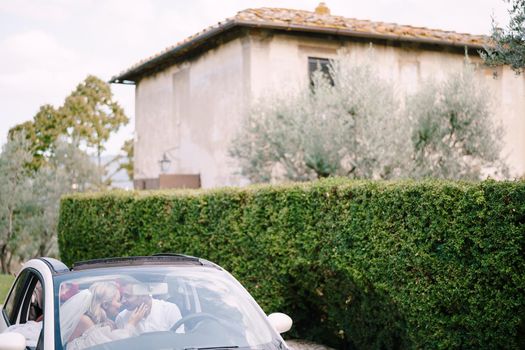 Beautiful bride and groom leaning forehead to forehead in a convertible in front of the old villa in Italy, in Tuscany, near Florence