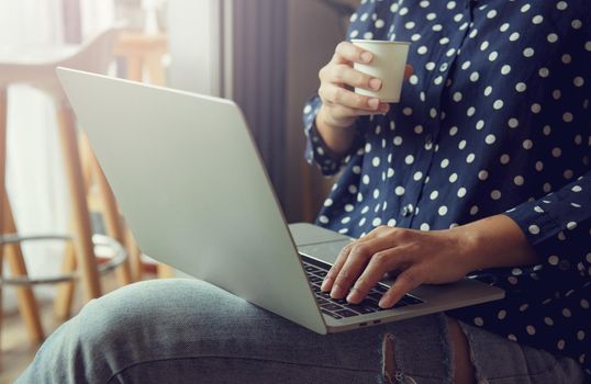 Young woman relaxing and drinking cup of hot coffee or tea using laptop computer in the cafe. Cozy office workplace, remote work,E learning Concept.