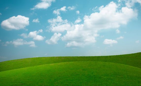 Landscape view of green grass on slope with blue sky and clouds background.