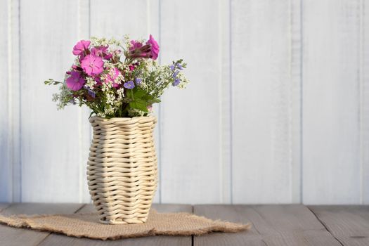 Bouquet of wildflowers in a wicker vase on a wooden table.
