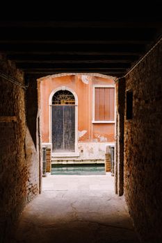 A look from the darkness at the light, at the old scratched door on the peach-colored wall near the water in the canal.