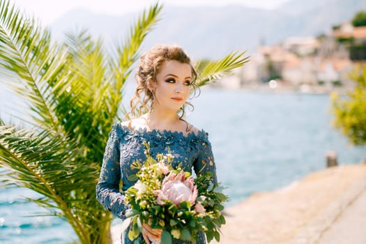 The bride in a stylish gray dress stands with wedding bouquets on the pier near old town of Perast, close-up. High quality photo