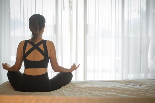 Woman doing yoga exercise on bed at home. Morning workout in bedroom. Healthy and sport lifestyle.