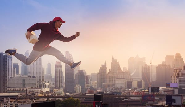 Delivery man holding cardboard boxes and jumping high on city background. Online Shopping and Express delivery Concept.